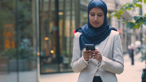Muslim-Businesswoman-Checking-Messages-On-Mobile-Phone-Standing-Outside-Office-In-City-2
